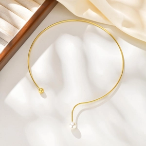 Détail du collier ras du cou doré avec perle asymétrique et boule métallique design minimaliste
