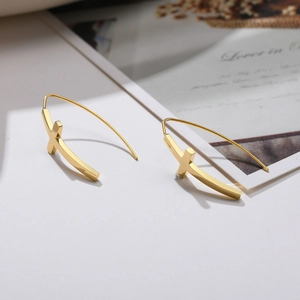Vue détaillée de boucles d'oreilles croix dorées polies sur un support minimaliste