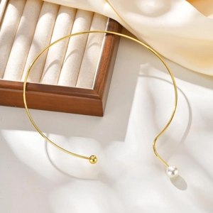 Gros plan du collier ras du cou doré asymétrique orné d'une perle blanche et d'une bille