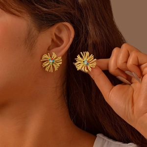 Boucles d'oreilles soleil dorées avec strass colorés portées sur fond marron élégant