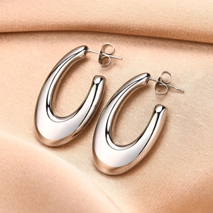 Macro shot of silver U-shaped chunky stainless steel earrings on pink silk fabric