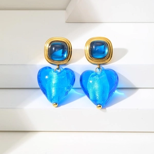 Détail de boucles d'oreilles vintage avec cœur bleu et clous dorés sur socle blanc
