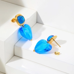 Détail de boucles d'oreilles cœur dorées avec incrustation en verre bleu sur socle