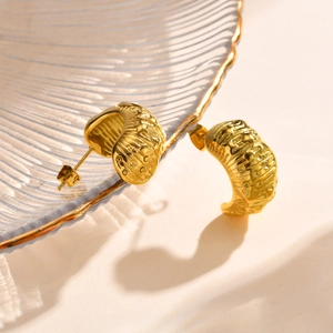 Macro view of 18K gold textured C-shape earring with embossed lava pattern on a glass tray