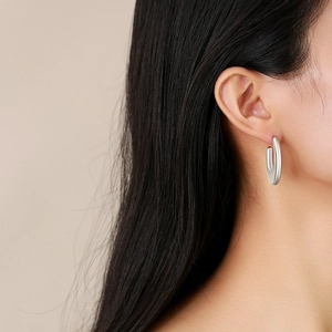 Detailed close-up of a silver-toned U-shaped geometric hoop earring worn by a model