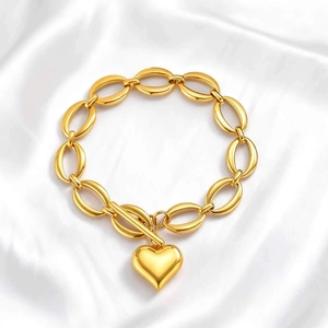 Détail d'un bracelet doré avec fermoir à bascule et pendentif cœur sur soie blanche