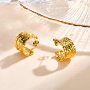 Detail of 18K gold C-shaped earrings with unique hammered texture on a beige surface