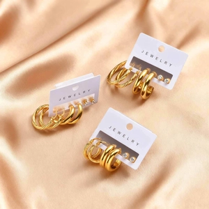 Three pairs of gold stainless steel hoop earrings and zircon studs on satin background