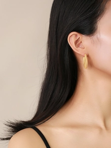 Close-up of model wearing gold hollow geometric hoop earrings with a matte satin finish