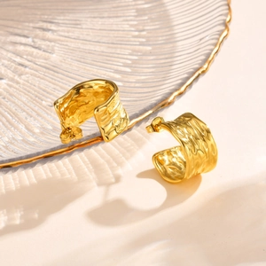 Close-up of gold 18K plated C-shaped earrings with hammered texture on shell tray