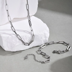 Close-up of matte silver paperclip chain necklace and bracelet on white stone