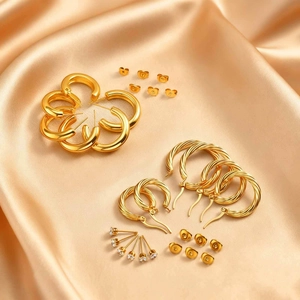 Flat lay of gold stainless steel twist hoops and zircon studs set on champagne satin fabric