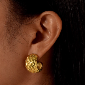 Macro shot of gold C-shaped earrings with embossed diamond texture on model's ear