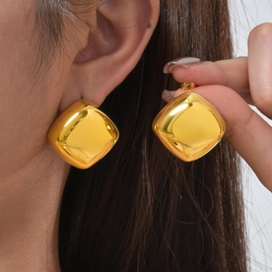 Macro shot of large square gold stud earrings with a polished mirror finish on a model