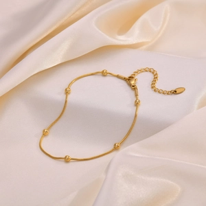Elegant gold stainless steel snake chain anklet with polished beads on silk background