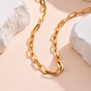 Close-up of golden paperclip chain necklace on white stones and beige background