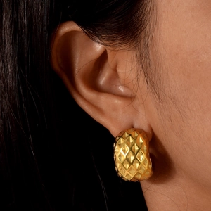 Detailed view of women wearing textured C-shaped 18K gold earrings with rhombus patterns