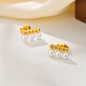 Detail of French style gold earrings with three pearls and textured bar on silk fabric