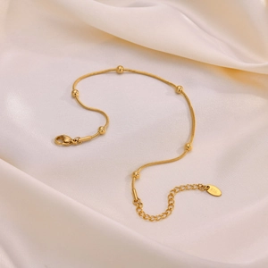 Macro view of gold snake chain anklet with beads and k18 engraving on silk fabric