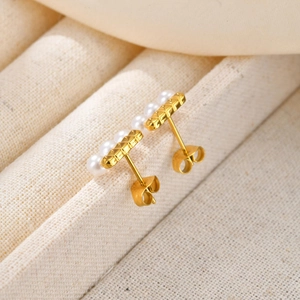 Macro shot of gold stud earrings featuring small pearls and a quilted metal texture design