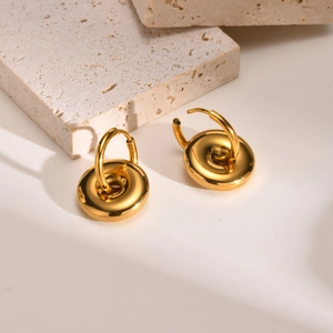 Macro detail of gold-plated geometric hoop earrings with polished donut pendants