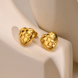 Détail de boucles d'oreilles cœur dorées tressées sur un support d'exposition moderne