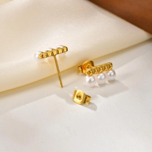 Detailed close-up of gold stud earrings featuring three pearls and textured metal bar