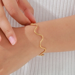 Close-up of a stylish gold wave-shaped open cuff bracelet worn on a woman's wrist