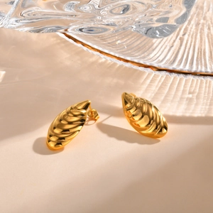 Macro detail of 18K gold-plated spiral wave stud earrings with shell texture and shadows