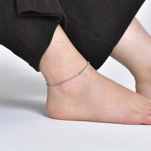 Detail of minimalist silver snake chain anklet with small beads on female model ankle