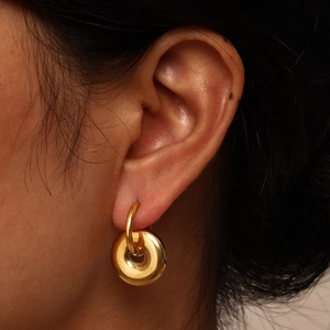 Close-up of golden geometric donut hoop earring showing the high-polished mirror finish