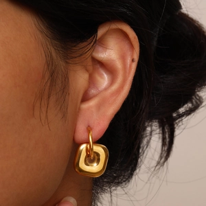 Close-up of a model wearing high-polish gold geometric square drop earrings in stainless steel