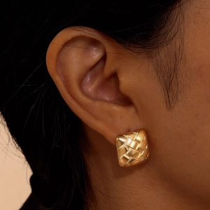 Boucles d'oreilles carrées tressées dorées portées par un mannequin avec texture