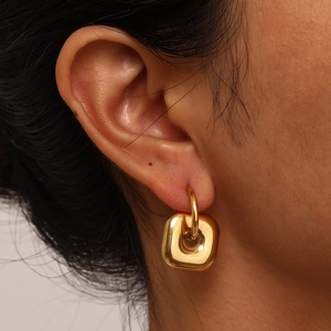 Close-up of golden geometric square hoop earring with high-polish finish on model's ear