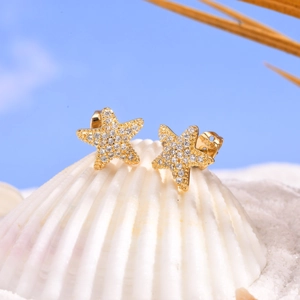 Golden starfish stud earrings with white zircons on a white seashell background
