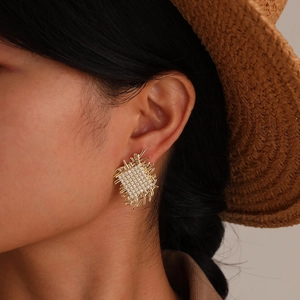 Close-up of woman wearing gold woven square stud earrings with zircons and straw hat