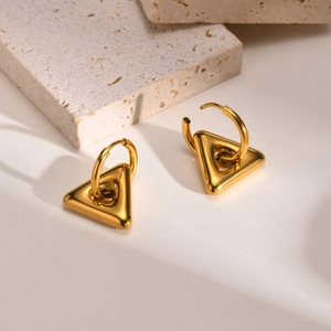 Close-up of golden geometric triangle hoop earrings on a textured stone display