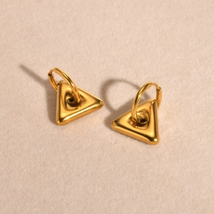 Detail of gold geometric triangle hoop earrings on a textured cream fabric background