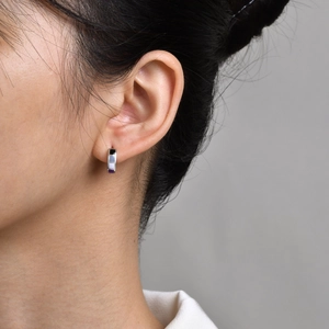 Macro detail of stainless steel hoop earring with colorful geometric enamel inlays on model