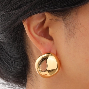 Close-up of a model wearing large golden geometric earrings with irregular teardrop cutouts