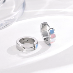 Detailed close-up of silver huggie earrings with colorful enamel inlay on white display