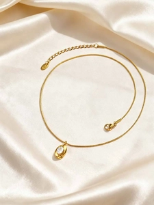 Detail of gold snake chain necklace with oval zircon pendant on champagne satin fabric