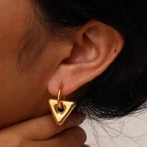 Macro view of a gold geometric triangle pendant earring worn on a model's earlobe