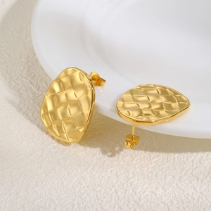 Detailed view of gold irregular oval earrings with quilted texture on ceramic plate