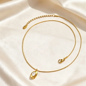 Golden stainless steel snake chain necklace with oval white zircon pendant on silk background