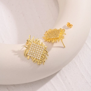 Golden woven stud earrings with sparkling cubic zirconia on a white ceramic display plate