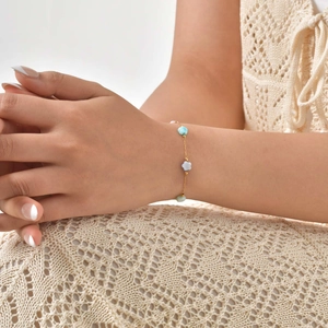 Close-up of a gold chain bracelet with blue and white shell flower charms on a wrist