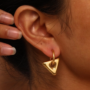 Macro shot of minimalist gold geometric triangle drop earring worn on a model's ear