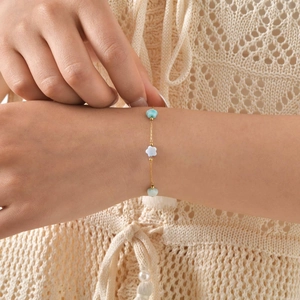 Detail of a thin gold chain bracelet with blue and white shell flower charms on a model