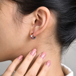 Macro shot of silver huggie earring with colorful stripes on earlobe profile